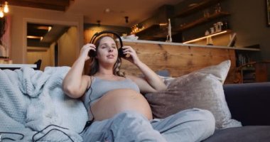 Pregnant woman listening to music and putting ear phone on tummy for the baby to listen. High quality 4k footage