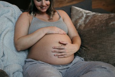 Anne şefkatle karnına bakıyor ve dairesindeki kanepesinde gülümsüyor. Yüksek kalite fotoğraf
