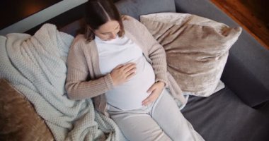Ağır hamile bir kadın kanepesinde oturup bebek yumrusunu okşuyor. Yüksek kalite 4k görüntü