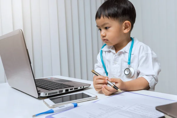 Menino Uniforme Médico Segurando Uma Caneta Olhar Para Laptop Mesa — Fotografia de Stock