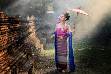 Taylandlı güzel bir kadın. Geleneksel giyinmiş. Duman ve sisin ortasında kırmızı şemsiyeli..