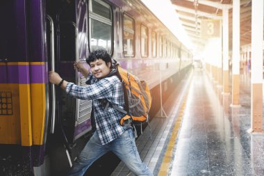 Asian man traveler with backpack is stepping up the train in train station.