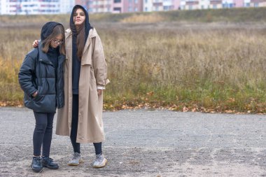 Sonbahar elbiseli iki kız şehrin ıssız bir köşesinde yan yana durur.