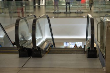 A deserted escalator fenced with a glass fence in a shopping center leads to the lower floor