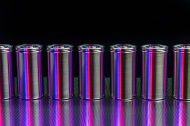 Bir paket yeni yüksek kapasiteli lityum iyon hücresi. Çelik bir yüzeydeki yeni bataryaların prototipi. Siyah arka planda kırmızı ve mavi ışıkla aydınlatılmış.