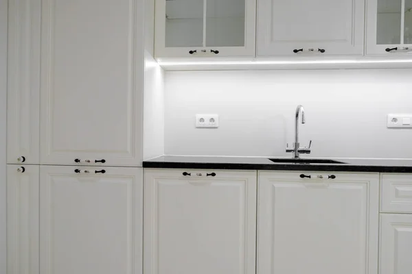 Μοντέρνα και κομψή κουζίνα με λευκά συρτάρια και ντουλάπια, μαύρο μαρμάρινο πάγκο και ενσωματωμένο νεροχύτη με ασημί βρύση — Φωτογραφία Αρχείου