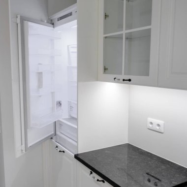 Beyaz çekmeceleri ve dolapları olan modern ve zarif bir mutfak, siyah mermer tezgah ve gümüş musluklu lavabo.