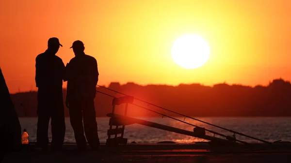 Gün batımında iskelede iki balıkçının silueti.