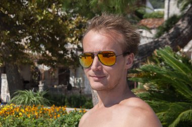 Yakışıklı, beyaz tenli, güneş gözlüklü, modern saç kesimli, Avrupa 'nın tropikal manzaralı genç adamı.. 