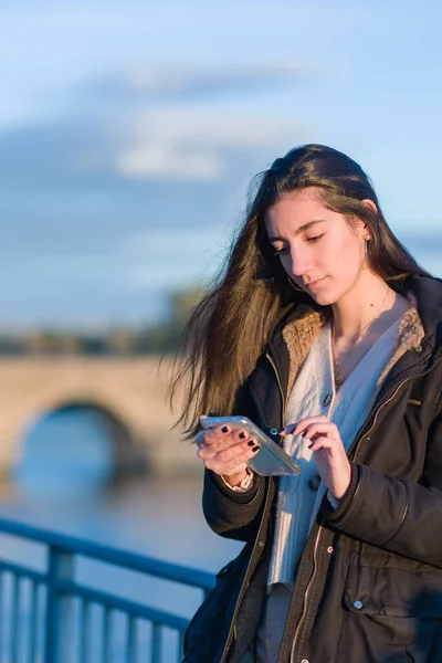 İspanyol genç kadın Toledo, Tajo Nehri yakınlarındaki sosyal ağlar için akıllı telefon kullanıyor. Soğuk kış stili — Stok fotoğraf