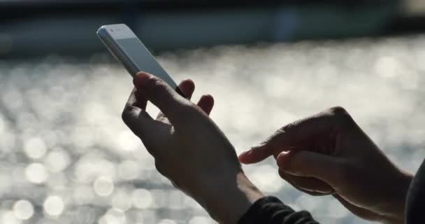 4k Дівчина, що використовує смартфон на узбережжі, ігристе поверхню води . — стокове відео