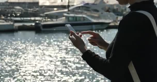 4 k A flicka med en smartphone på seaside, yacht & segling i hamnen. — Stockvideo