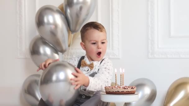 Мальчик празднует день рождения, у ребенка вечеринка в честь дня Б. Мальчик задувает свечи на праздничном торте. Празднование, белый минималистский интерьер. — стоковое видео