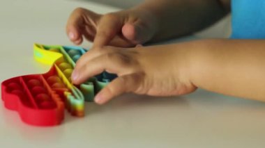 Çocuk gökkuşağıyla oynuyor Pop it modget toy. Stres önleyici çocuklar oyunu. Çocuklar için kullanılan silikon oyuncaklar stresi azaltmak ve el motor becerilerini geliştirmek için kullanılır. Köpüklü renkli el oyuncağı.