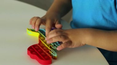 Çocuk gökkuşağıyla oynuyor Pop it modget toy. Stres önleyici çocuklar oyunu. Çocuklar için kullanılan silikon oyuncaklar stresi azaltmak ve el motor becerilerini geliştirmek için kullanılır. Köpüklü renkli el oyuncağı.
