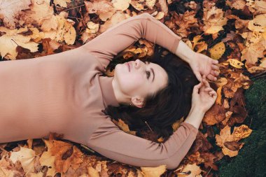 Çekici genç esmer kadın, sarı sonbahar yapraklarının üzerine uzanıyor. Yapraklı kız. Yukarıdan bak, sonbahar parkında..