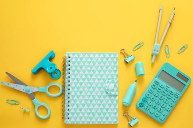 Sarı arkaplanda mavi kırtasiye malzemeleri ve metin için boş alan. Yaratıcı, okul malzemeleriyle renkli bir geçmişi var. Flatlay ile kopyalama alanı, üst görünüm. İşaretleyici, kalem, ataç, makas