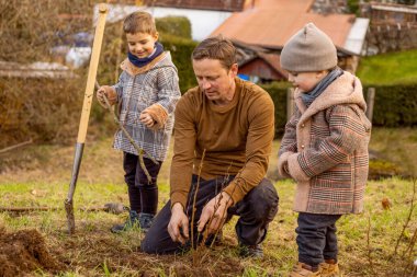 Çocuklu bir adam bahçeye ağaç diker. Doğa, çevre ve ekoloji kavramı. Baba ve çocukları dışarıda, ailece vakit geçiriyorlar..