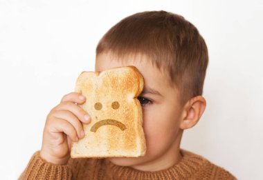Çocuklar ve glüten. Kızarmış ekmeği ve üzgün emojisi olan anaokulu çocuğu. Çocukların glüten duyarlılığı.