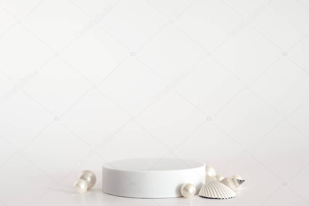 White podium with pearls and shells on the white background, simple geometric form. Podium for product, cosmetic presentation. Creative mock up. Pedestal or platform for beauty products.