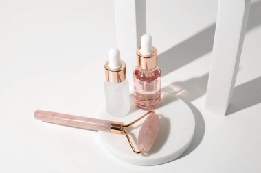 Masaj kuvars silindiri ve beyaz arka planda iki cam şişe şeffaf sıvı jel. Damla şişesi, hyaluronik asit, yağ, serum. Yüz masajı ve rahatlama. Gua Sha masaj aletleri.