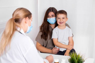 Küçük oğluyla birlikte genç esmer kadın çocuk doktorunda danışmanlık yapıyor. Doktor, çocuk ve anne koronavirüs ve grip salgını sırasında maske takıyor. Virüs koruması. Covid 19.