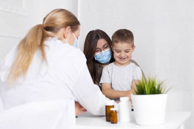 Küçük oğluyla birlikte genç esmer kadın çocuk doktorunda danışmanlık yapıyor. Doktor, çocuk ve anne koronavirüs ve grip salgını sırasında maske takıyor. Virüs koruması. Covid 19.