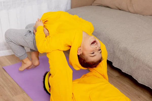 Un joven con un niño haciendo ejercicios de fitness en casa. Padre e hijo divirtiéndose durante el deporte. Papá y su hijo haciendo entrenamiento. Deporte, yoga. Entrenamiento en el apartamento. Vida sana, familia. —  Fotos de Stock