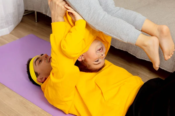 Young man with little boy doing fitness exercises at home. Father and son having fun during sport. Dad and his child making training. Sport, yoga. Workout in the apartment. Healthy lifestyle, family. — Stock Photo, Image