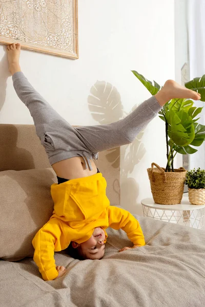 Kleiner kaukasischer Junge turnt im Wohnzimmer Handstandübung. Kind steht auf dem Kopf und hat Spaß. Sport zu Hause. Training in der Wohnung. Gesunder Lebensstil. — Stockfoto