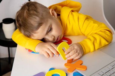 Küçük çocuk evde dizüstü bilgisayarla alfabe ve rakamları internetten öğreniyor. Çocuk üzgün ve yorgun. Olumsuz duygular, stres, zihinsel sorunlar. Çocuklar için ev eğitimi ve uzaktan eğitim.