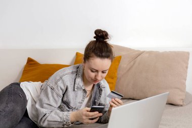 Genç esmer kadın dizüstü bilgisayarında internette sörf yaparken gülümsüyor ve elinde kredi kartıyla internetten bir şeyler almaya çalışıyor. Evde kolay online alışveriş, e-ticaret. İçerisi çok rahat..