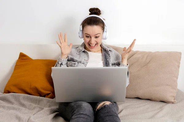 Mladá běloška se sluchátky na posteli s laptopem. Dívka používající notebook surfovat na internetu, číst zprávy, dívat se na film, studovat. Překvapené, pozitivní emoce. Vyhrál cenu online. — Stock fotografie