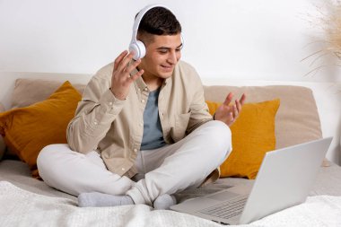 Gündelik giysileri olan genç bir adam dizüstü bilgisayarla yatakta oturuyor. İnternette çalışmak için defteri kullanan, arkadaşlarını arayan, ailesiyle konuşan bir adam. Uzaktan öğrenme, video çağrısı. Evde dinleniyorum..