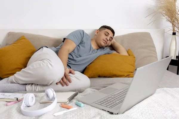 Mladý muž je velmi unavený po studiu a usnul. Muž s neformálním oblečením ležící doma na posteli s notebookem. Používání e-learningové platformy. Vzdělání na dálku. Útulný interiér. Termín. — Stock fotografie