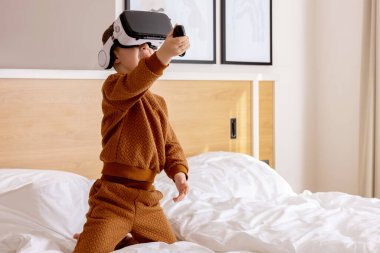 Evde VR kulaklığı takmış, interaktif video oyunu oynayıp sanal gerçekliği keşfeden sevimli bir çocuk. VR gözlük takan sevimli bir çocuk. Gelecek, cihazlar, teknoloji, eğitim online.