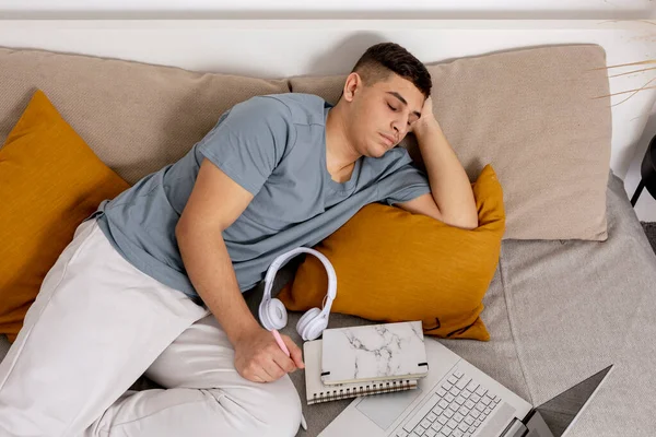 Mladý muž je velmi unavený po studiu a usnul. Muž s neformálním oblečením ležící doma na posteli s notebookem. Používání e-learningové platformy. Vzdělání na dálku. Útulný interiér. Termín. — Stock fotografie