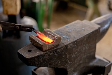 Isıtılmış metal ve örsün yakın görüntüsü. Demirhanede el yapımı metal ürünlerinin üretim sürecindeki demirci. Demirci çekiçle metal dövüyor. Metal endüstrisi, eski meslek