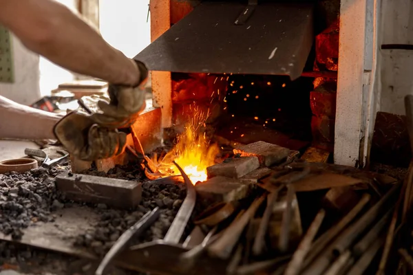 The blacksmith in production process of metal products, handmade in the forge. Craftsman heats metal in the fire. Metal industry, old profession