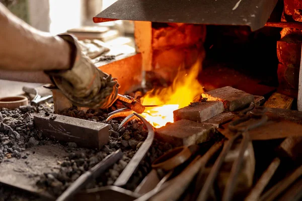 The blacksmith in production process of metal products, handmade in the forge. Craftsman heats metal in the fire. Metal industry, old profession