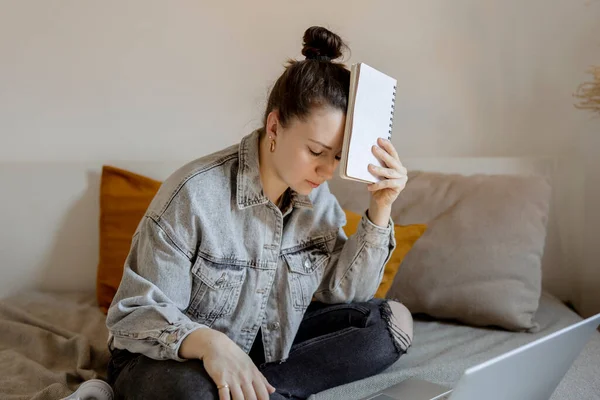Young beautiful woman with casual clothes sitting on the bed at home with laptop computer and studying. Girl is sad and tired. Negative emotions, stress, mental problems, deadline. Distance education