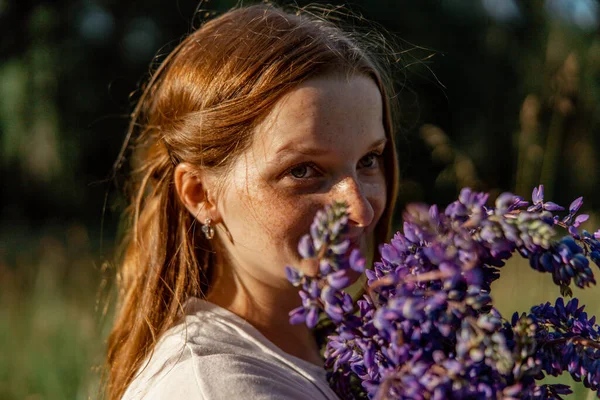 Close up portrait of young beautiful redhead woman with freckles, wearing white dress, posing in the nature. Girl with red hair holding flowers. Natural beauty. Diversity, individual uniqueness