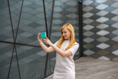 Genç sarışın kadın, takipçileri için akıllı telefondan selfie çekiyor. Etkileyici genç bir kız. İnternette popülerlik, internette arkadaşlar. Sosyal medya hesabı için içerik oluşturan güzel kız