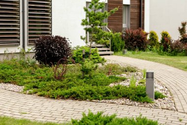 Various plants and stones in front of modern house, front yard. Landscape design. Beautiful garden. Modern urban living residences with private courtyards. Green outdoor facilities, lawn. Garden care