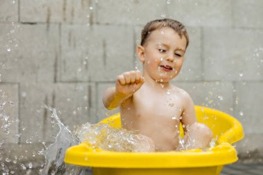 Cute little boy bathing in yellow tub outdoors. Happy child is splashing, playing with water and having fun. Summer season and recreation. Staying cool in the summer heat. Water fun in backyard