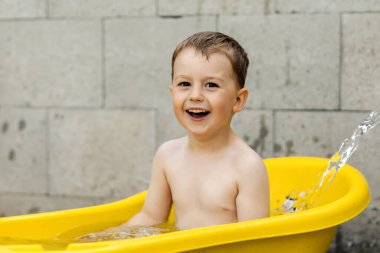 Cute little boy bathing in yellow tub outdoors. Happy child is splashing, playing with water and having fun. Summer season and recreation. Staying cool in the summer heat. Water fun in backyard