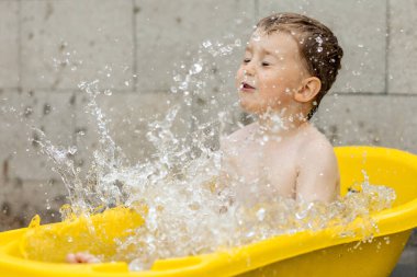 Cute little boy bathing in yellow tub outdoors. Happy child is splashing, playing with water and having fun. Summer season and recreation. Staying cool in the summer heat. Water fun in backyard