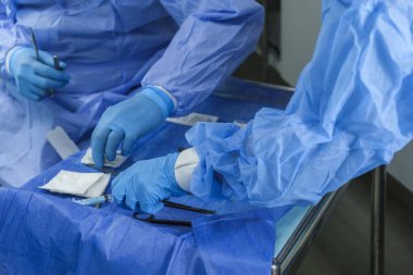 Ameliyathanede, ameliyat sırasında, lateks eldiven takan doktor ve hemşire masadan tıbbi gereçleri alıyorlar. Elleri cerrahi aletlerle kapatın.