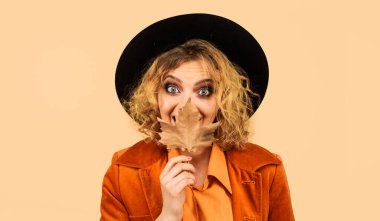 Güz yapraklı, siyah şapkalı güzel, şaşkın genç bir kadın. Sonbahar yeşillikleri olan moda kızı. Sezon indirimi.