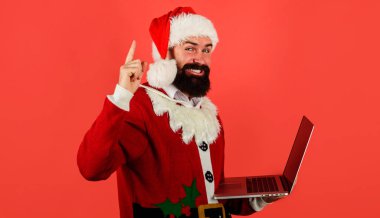 Bilgisayarlı Noel Baba. Noel Baba kostümü giymiş sakallı iş adamı ve elinde bilgisayar var. İnternetten alışveriş. Dijital aygıt.